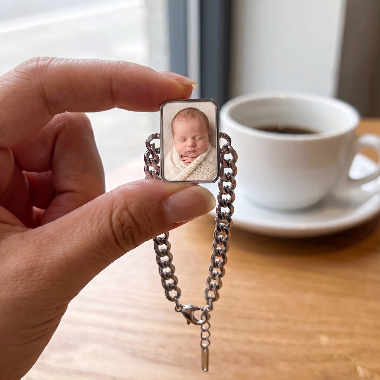 The silver cushion-cut photo charm held between two fingers, showing its real small size with a newborn baby's photo | SKU: TPH-CUSB-SILVER