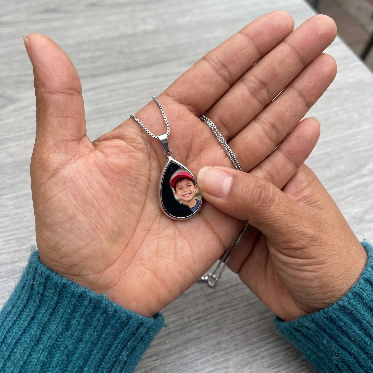 Thumb warming the silver teardrop pendant: the hidden photo appears under the thumb while the rest stays black | SKU: TPH-DRPN-SILVER
