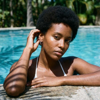 Thumbnail for Tiny Huggie Hoops in Silver, worn by a tropical pool | SKU: 41002-silver