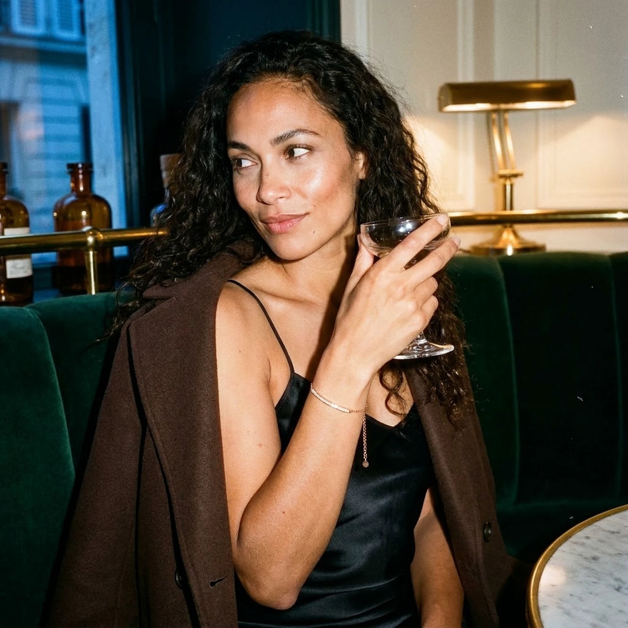 Woman wearing the rose gold Crystal Bar Bracelet in a bar, green velvet and warm lamplight